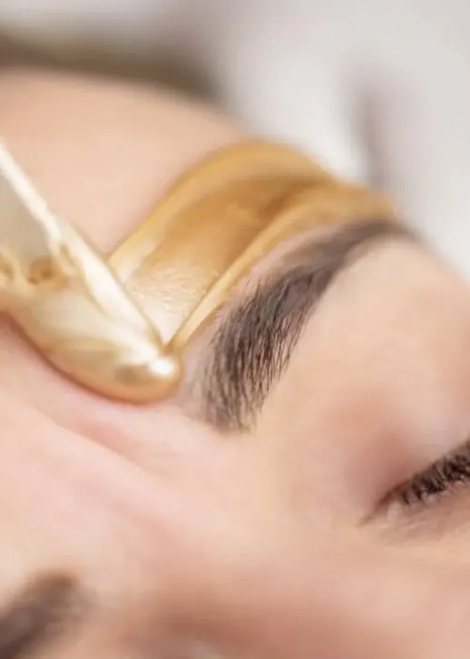 Warm golden wax applied along an eyebrow with a wooden spatula